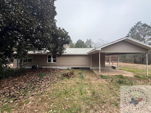 back of house with central AC, a lawn, metal roof, and a carport