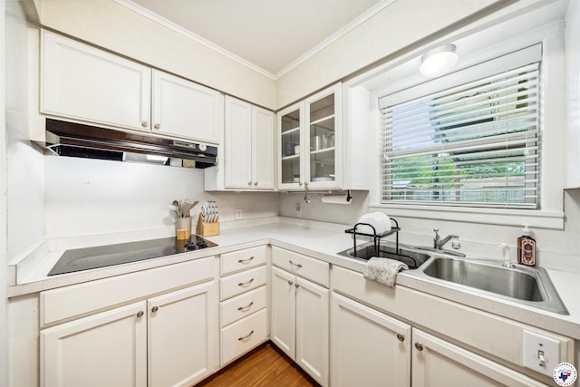 kitchen with under cabinet range hood, glass insert cabinets, black electric stovetop, light countertops, and ornamental molding