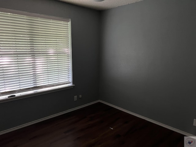 spare room featuring dark wood-type flooring and a textured ceiling