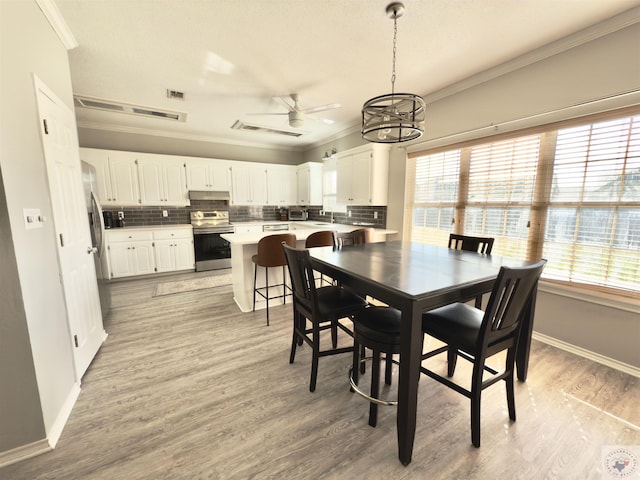 dining room featuring visible vents, light wood-style flooring, ornamental molding, and a healthy amount of sunlight