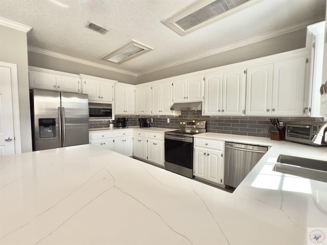 kitchen with appliances with stainless steel finishes, under cabinet range hood, visible vents, white cabinets, and decorative backsplash