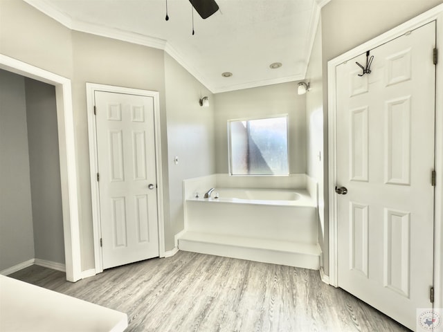 bathroom with crown molding, wood finished floors, a bath, baseboards, and ceiling fan