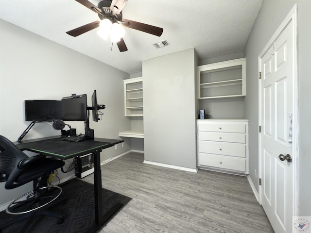 office space featuring baseboards, a textured ceiling, visible vents, a ceiling fan, and wood finished floors