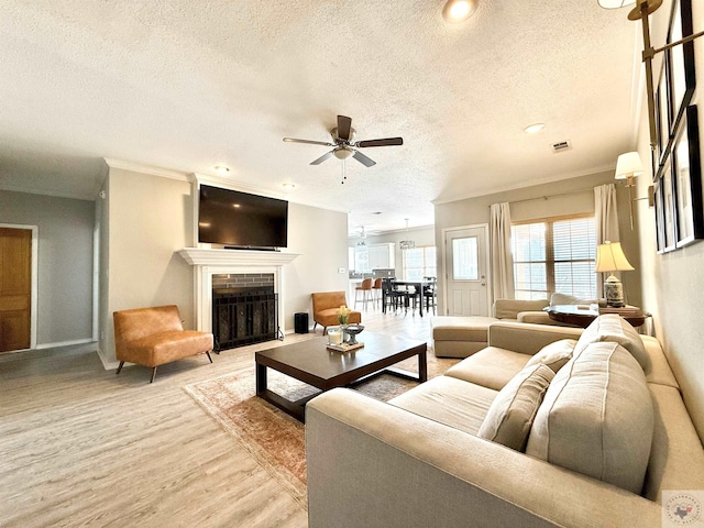 living area featuring crown molding, a textured ceiling, light wood-type flooring, visible vents, and ceiling fan