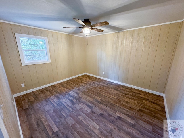 empty room featuring wood walls, dark wood-type flooring, crown molding, and ceiling fan