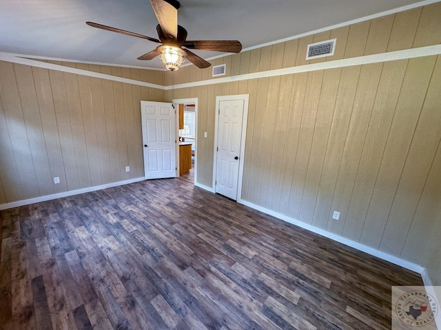 unfurnished bedroom with crown molding, wood walls, ceiling fan, and dark hardwood / wood-style flooring