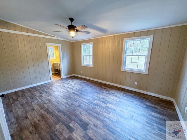 unfurnished bedroom featuring wood walls, dark wood-type flooring, ensuite bath, and ceiling fan