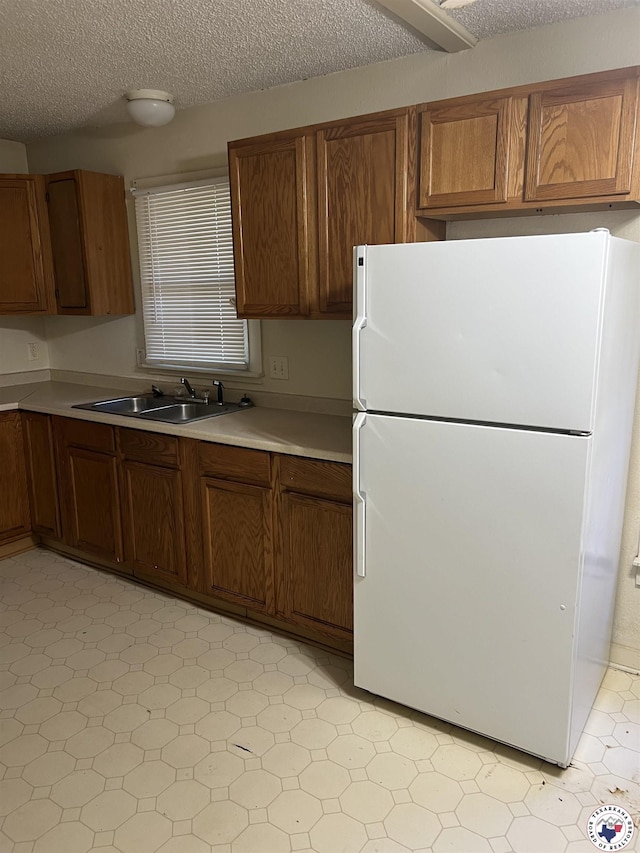319 Crestview Rd, Texarkana, TX 75501 - kitchen featuring freestanding refrigerator, a sink, light countertops, brown cabinets, and a textured ceiling