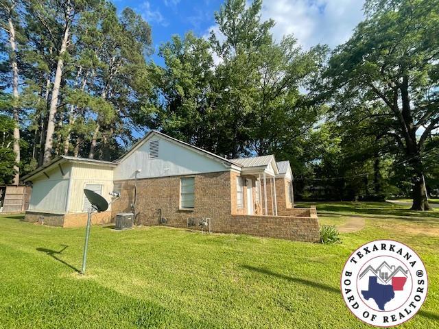 104 Pecan St, Atlanta, TX 75551 - view of side of home with a yard, brick siding, and central AC unit