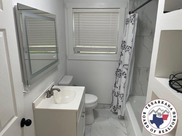 104 Pecan St, Atlanta, TX 75551 - full bathroom with toilet, vanity, marble look tiles, and shower / bath combo with shower curtain