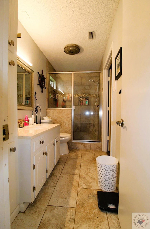 bathroom with a textured ceiling, toilet, vanity, and walk in shower