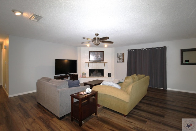 living room with a fireplace, a textured ceiling, dark hardwood / wood-style floors, and ceiling fan