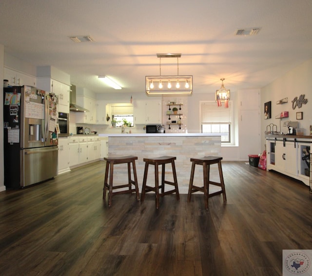 kitchen featuring white cabinets, dark wood-type flooring, pendant lighting, stainless steel appliances, and wall chimney exhaust hood