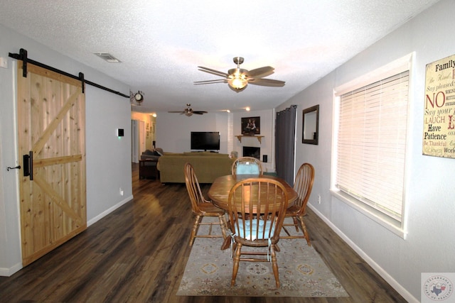 dining area with ceiling fan, dark wood-type flooring, a barn door, a fireplace, and a textured ceiling