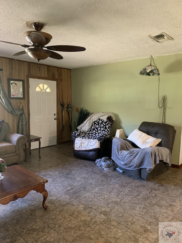 living room with ceiling fan, a textured ceiling, and wood walls