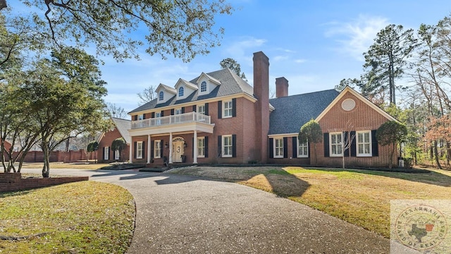 colonial inspired home featuring brick siding, covered porch, a balcony, driveway, and a front lawn