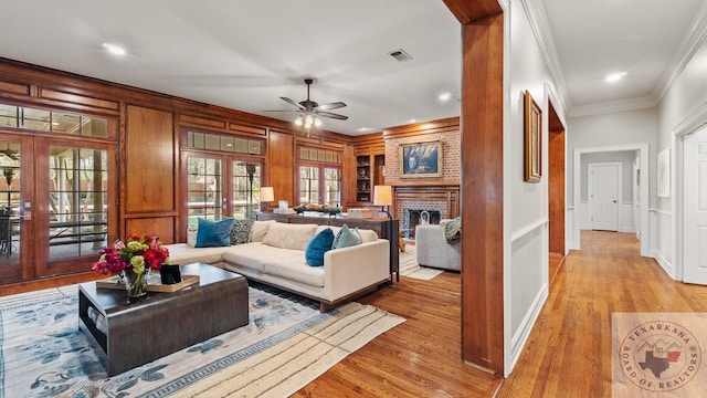 living room with light wood-style flooring, a fireplace, visible vents, french doors, and crown molding