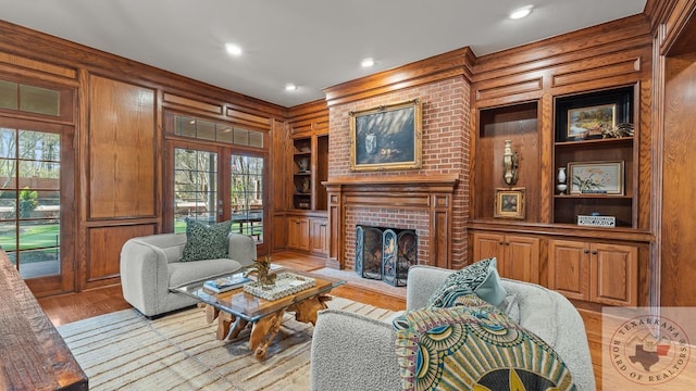 living area with wooden walls, light wood-style flooring, a brick fireplace, built in shelves, and recessed lighting