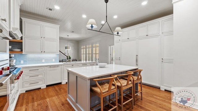 kitchen with a kitchen island, visible vents, white cabinets, light countertops, and ornamental molding