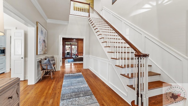 stairs with ornamental molding, wainscoting, wood finished floors, and a decorative wall