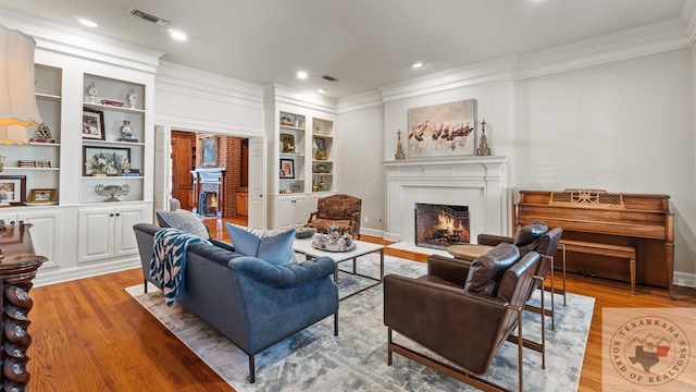 living room with ornamental molding, a lit fireplace, light wood-style flooring, and visible vents