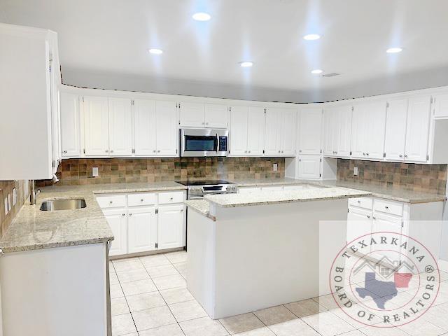 kitchen featuring light tile patterned floors, white cabinetry, appliances with stainless steel finishes, and a kitchen island