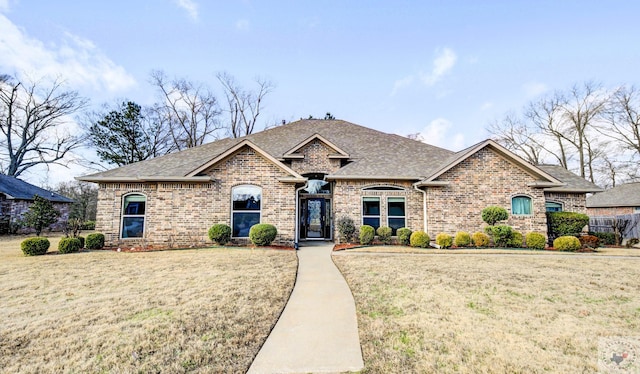 french country style house featuring brick siding, roof with shingles, and a front yard