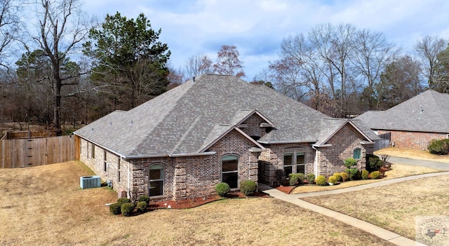 view of front of property with a shingled roof, fence, central air condition unit, a front lawn, and brick siding