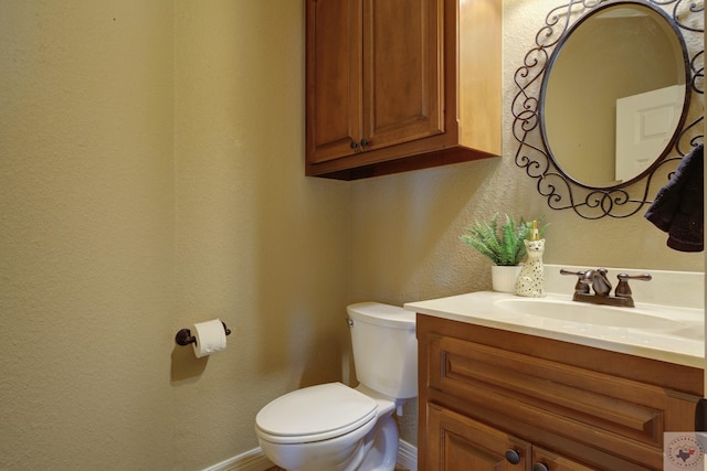 half bath featuring a textured wall, vanity, toilet, and baseboards