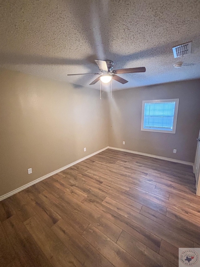 empty room featuring ceiling fan, dark wood-type flooring, and a textured ceiling