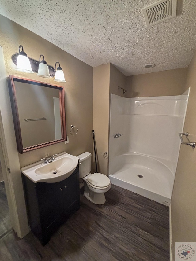 bathroom featuring a shower, hardwood / wood-style flooring, a textured ceiling, toilet, and vanity