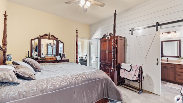 bedroom featuring a barn door, ceiling fan, wooden walls, concrete flooring, and ensuite bath