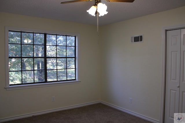 empty room featuring ceiling fan, dark colored carpet, and a textured ceiling