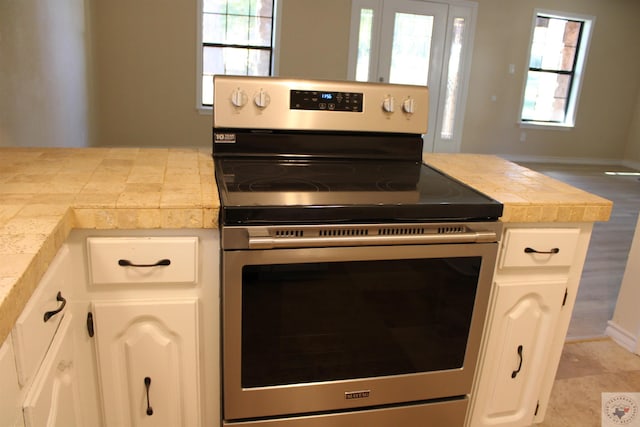 kitchen featuring electric stove, white cabinetry, tile counters, and a healthy amount of sunlight