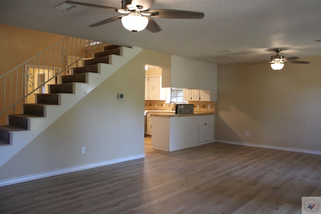 unfurnished living room with wood-type flooring, a textured ceiling, and ceiling fan