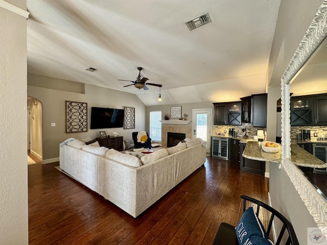 living room with dark wood-style floors, visible vents, lofted ceiling, arched walkways, and a tiled fireplace