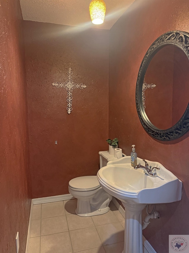 half bath featuring tile patterned floors, toilet, a sink, and a textured wall