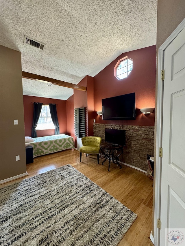 bedroom featuring lofted ceiling, wood finished floors, visible vents, and a textured ceiling