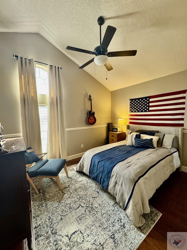 bedroom featuring a ceiling fan, a textured ceiling, wood finished floors, baseboards, and vaulted ceiling