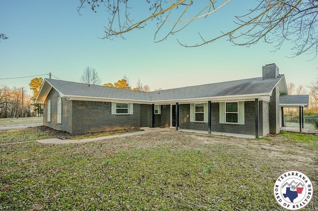 single story home with brick siding, a chimney, a shingled roof, and a front yard