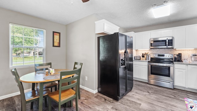 8809 N Kings Hwy, Texarkana, TX 75503 - kitchen with stainless steel appliances, tasteful backsplash, light wood-style flooring, white cabinetry, and a textured ceiling
