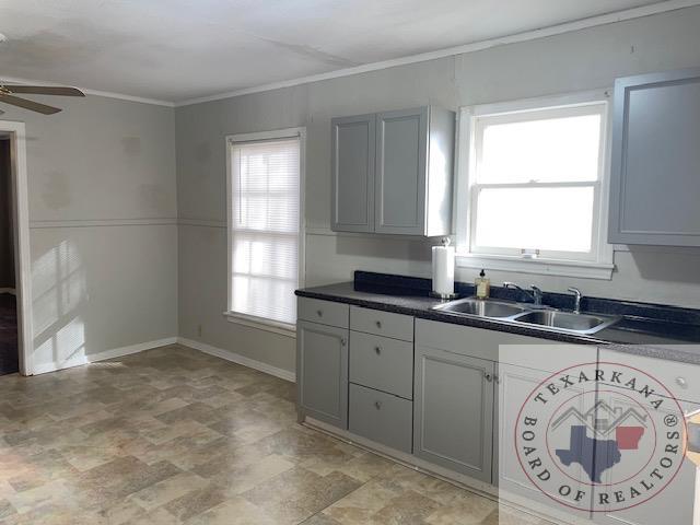 kitchen with dark countertops, baseboards, ceiling fan, ornamental molding, and a sink