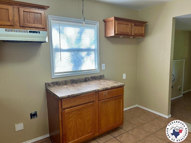 704 Florence St, Atlanta, TX 75551 - kitchen with under cabinet range hood, brown cabinetry, light tile patterned floors, baseboards, and dark countertops