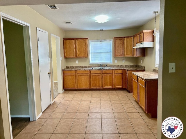 704 Florence St, Atlanta, TX 75551 - kitchen with brown cabinets, under cabinet range hood, a sink, pendant lighting, and light tile patterned floors