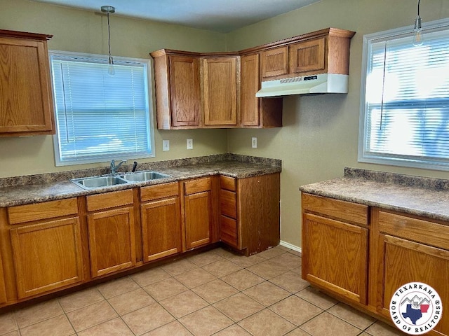 704 Florence St, Atlanta, TX 75551 - kitchen with under cabinet range hood, a sink, brown cabinets, dark countertops, and hanging light fixtures