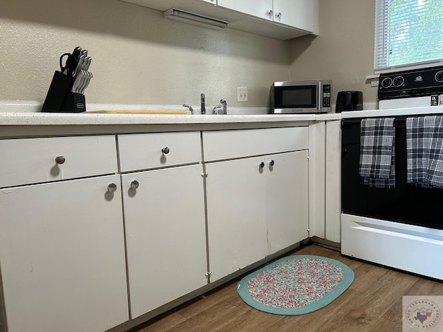 kitchen featuring hardwood / wood-style flooring, white cabinetry, and electric range oven