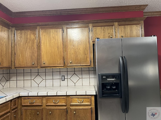 kitchen featuring decorative backsplash, a textured ceiling, stainless steel fridge, and tile counters