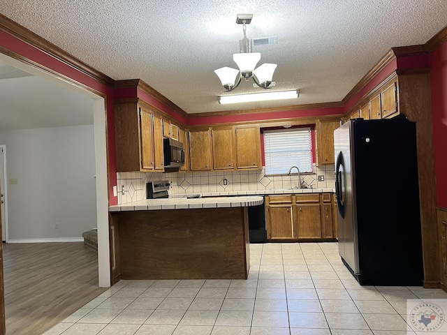 kitchen featuring pendant lighting, light tile patterned floors, tile countertops, black appliances, and a chandelier