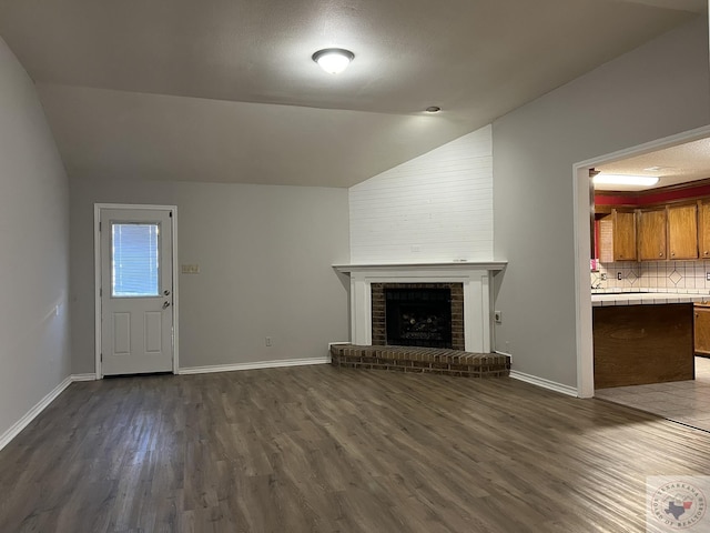 unfurnished living room featuring lofted ceiling, a textured ceiling, dark hardwood / wood-style floors, and a brick fireplace