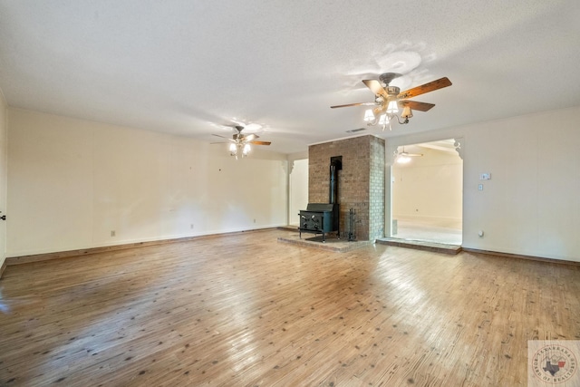 unfurnished living room featuring wood-type flooring, a textured ceiling, a wood stove, and ceiling fan